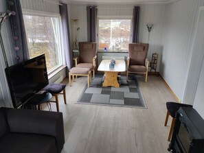 Un salon avec un téléviseur, deux fauteuils, une table et un canapé.