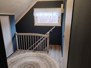 A staircase with a white railing, a small window with lace curtains, and a patterned rug. - Cozy house with beautiful view (Vestvågøy)