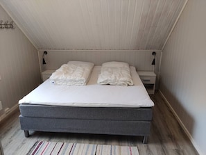 A single bed with a grey mattress and white bedding, two bedside tables with lamps, a striped rug, and a sloped ceiling.