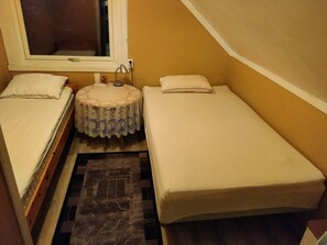 Une petite pièce étroite, avec deux lits simples, une table ronde recouverte d’une nappe en dentelle et une fenêtre.