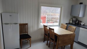 Ett kompakt kök med ett matbord, stolar, ett kylskåp och ett fönster med utsikt över en röd byggnad.