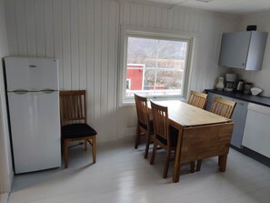 A compact kitchen with a dining table, chairs, a refrigerator, and a window with a view of a red building.