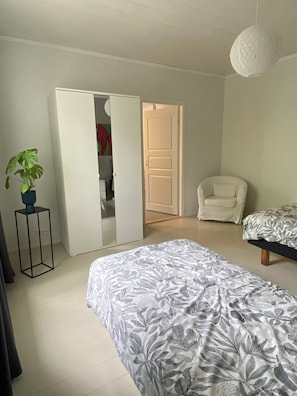 A bedroom with a bed, a chair, a wardrobe, and a potted plant.
