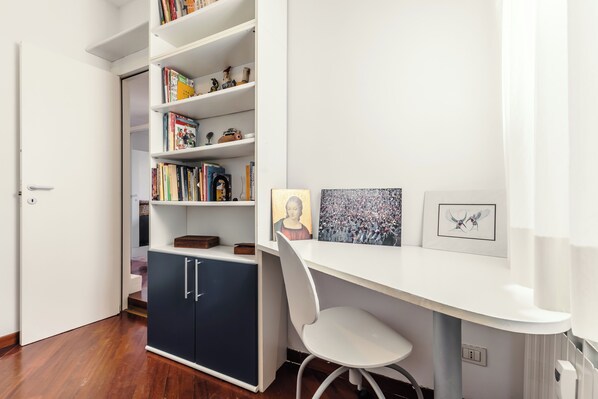 Ein Arbeitszimmer mit weißem Schreibtisch, Stuhl, Bücherregal und Schrank.