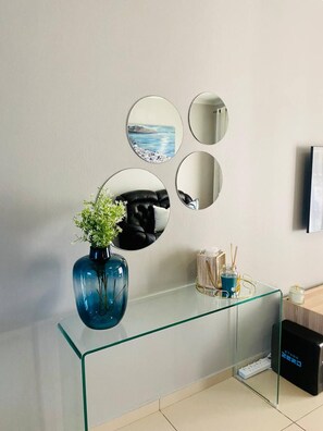 Ein modernes Badezimmer mit einem Glaswaschtisch, einer blauen Vase mit Grünpflanzen und einem Spiegel mit einem Küstenbild.