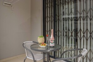 Ein runder Tisch mit einer Weinflasche, einer Obstschale und einem Korbkörbchen auf einem Balkon mit Metallstühlen.