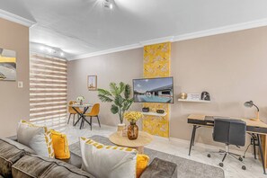 A modern living room with a sofa, coffee table, TV, and a desk with a chair. - A studio apartment close to Sandton and Rosebank (Sandton)