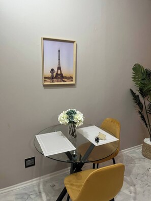 A round glass table with two yellow chairs, a vase with white flowers, a framed picture of the Eiffel Tower, and a small potted plant. - A studio apartment close to Sandton and Rosebank (Sandton)