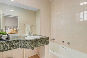 Ein Badezimmer mit Granitwaschtisch, zwei Waschbecken, einem Spiegel, einer Badewanne und einem Handtuchhalter.