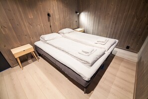 Una cama doble con cabecera de madera, dos mesitas de noche y una lámpara fijada a la pared.