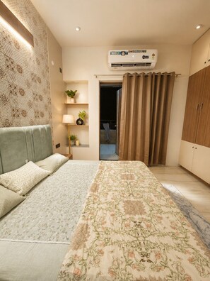 Un dormitorio con cama, mesita de noche, lámpara, planta en maceta, equipo de aire acondicionado y armario.