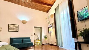 Un salon spacieux avec un plafond en bois, un canapé vert, un téléviseur à écran plat et une grande fenêtre avec des rideaux.