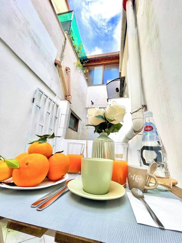 Ein Tisch mit Orangen, einer Kaffeetasse, einem Glas Orangensaft, einer Wasserflasche und einem Löffel auf einer blauen Tischdecke.