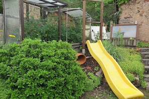 Ein Garten mit einer gelben Rutsche, grünen Büschen und einer Metallkonstruktion.