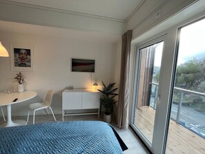 Habitació d'hotel amb llit, escriptori amb làmpada, cadira, planta en test i una finestra gran amb vistes.