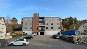 Un edificio de varios pisos con entrada central, zona de estacionamiento y árboles circundantes.