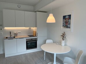 A modern kitchen with white cabinetry, a built-in oven, and a dining area with a round table and chairs. - Lofoten Studio Penthouse (Vågan)