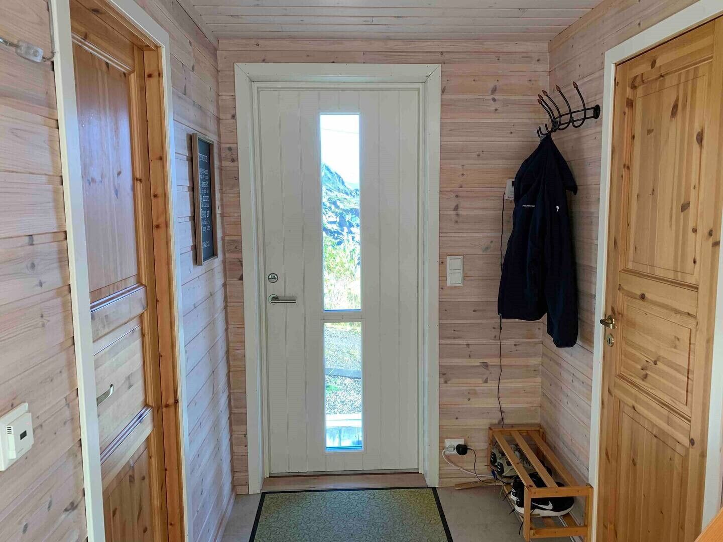 Un pasillo interior de madera con una puerta que da al exterior, un perchero y un banco.