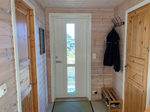 A wooden interior hallway with a door leading outside, a coat rack, and a bench.