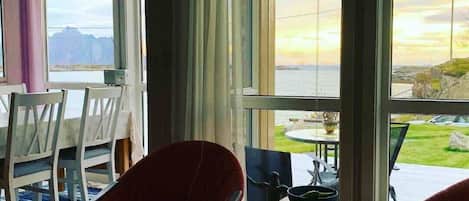 A room with a large window, a dining table, chairs, and a small table with a bowl.