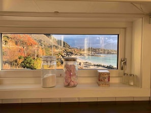 Ein Fenster mit Blick auf eine Küstenlandschaft, ein Regal mit Gläsern und einer dekorativen Schachtel.