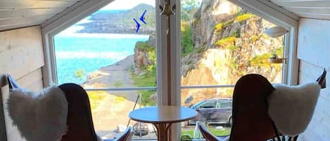 A room with a large window, two chairs, a small table, and a bell.