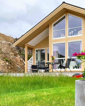 A modern house with a large glass window, a stone wall, and a grassy lawn.