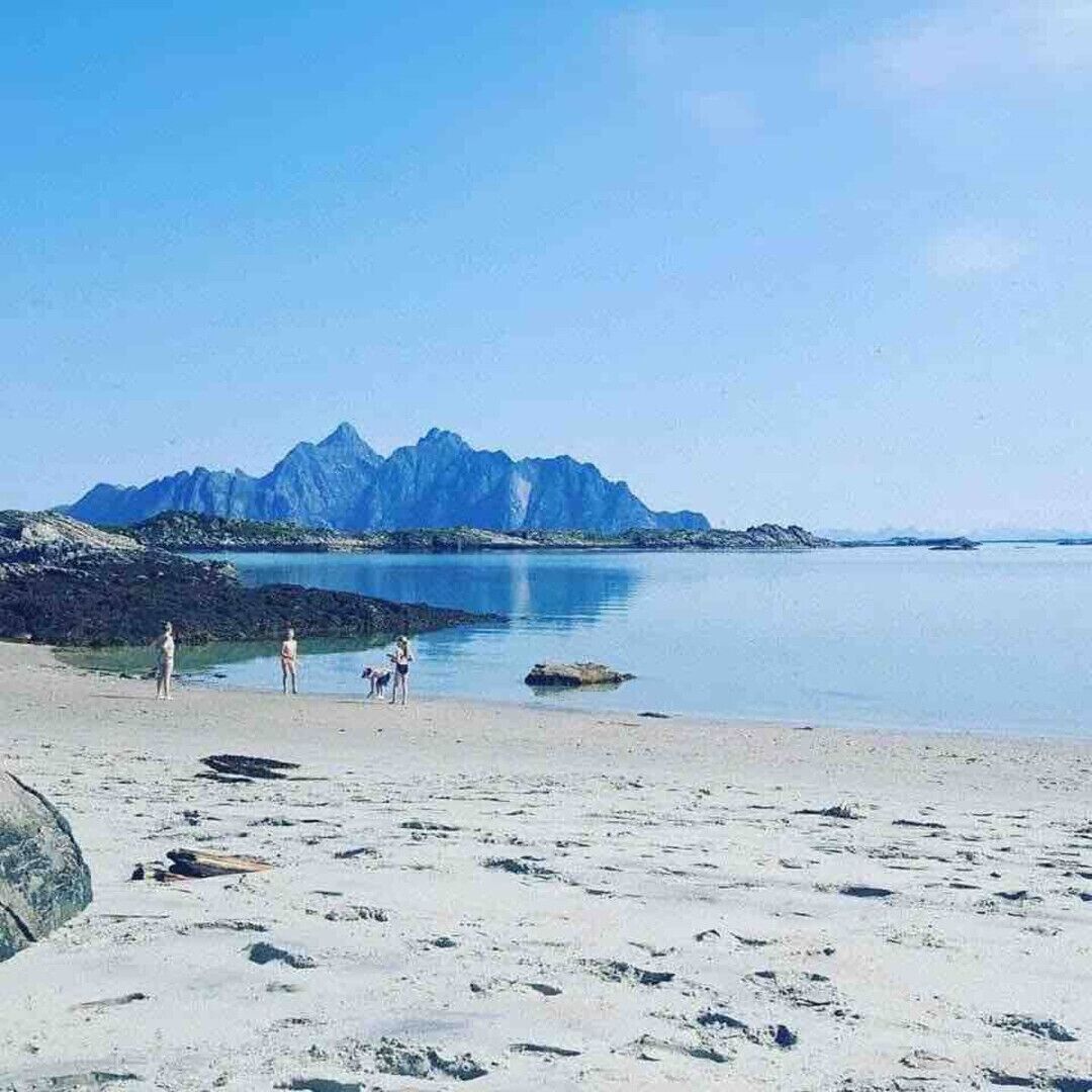 En strand med bjerge i baggrunden, en klar himmel og fodaftryk i sandet.