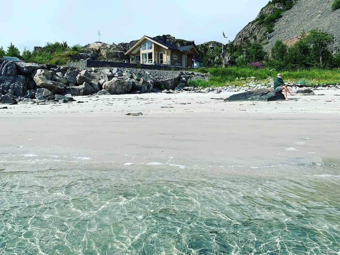 A beach with clear water, a house with a balcony, and rocky terrain.