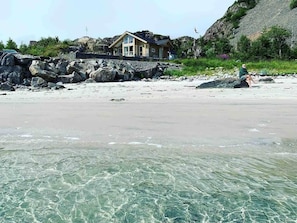 Ein Strand mit klarem Wasser, ein Haus mit Balkon und felsigem Gelände.
