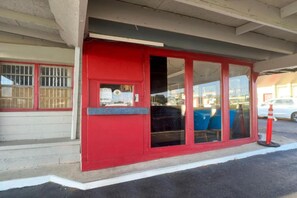A red building with large windows and a door, a parking lot, and a white car in the background. - King Bed|Smoking|Mobile AL (Mobile AL)