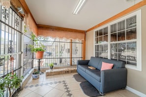 A sunlit balcony with a sofa, potted plants, and a view of the street.