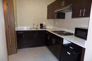 Una cocina compacta con armarios oscuros, una encimera blanca, una estufa y un microondas.