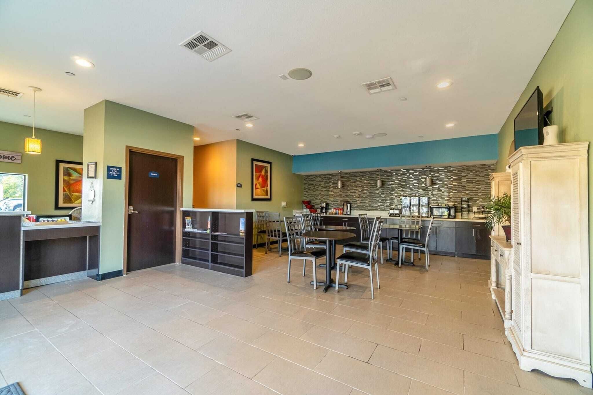 A spacious indoor area with a reception desk, a dining table with chairs, a kitchen area with a stone backsplash, and a large cabinet.