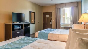 Ein Hotelzimmer mit zwei Betten, einem Fernseher, einem Schreibtisch mit Computer und einem Fenster mit Vorhängen sowie einer Lampe.