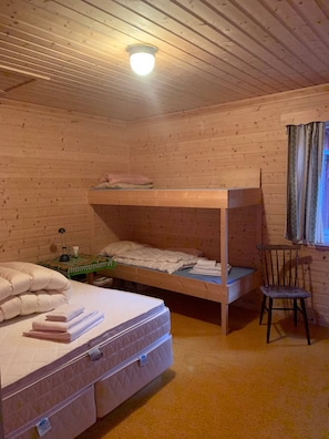 Quarto com beliche, escrivaninha com cadeira e janela com cortinas.