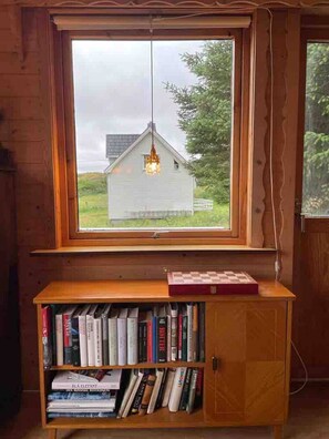 Une bibliothèque en bois remplie de livres, une fenêtre donnant sur une maison et un luminaire suspendu.