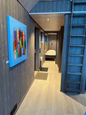 Ein Hotel-Flur mit Holzboden, einem Bett mit weißer Matratze, einem blauen Kunstwerk an der Wand und einer Holzleiter.