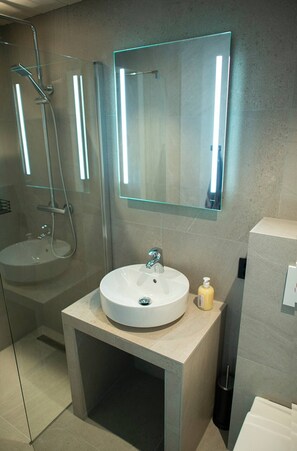 Ein modernes Badezimmer mit einer Glaskabine zur Dusche, einem runden Waschbecken und einem großen Spiegel.