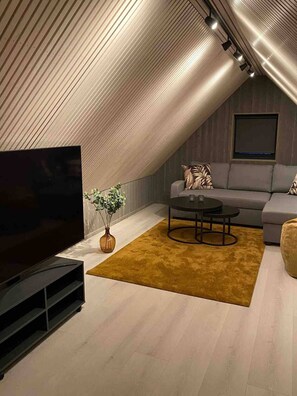 A modern loft bedroom with a sloped ceiling, a large flat-screen TV, a sofa, a coffee table, and a potted plant. - Spectacular view sea front Henningsvær (Vågan)
