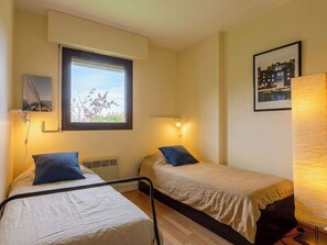 Ein Zimmer mit zwei Betten, einem Fenster, einem Wandregal, einem gerahmten Bild und einer Lampe.