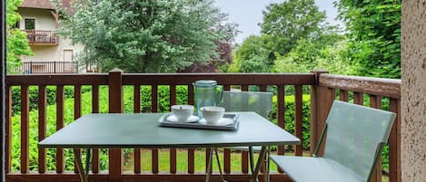 Un patio con una mesa y sillas, una jarra de vidrio y una bandeja con tazas y platitos.