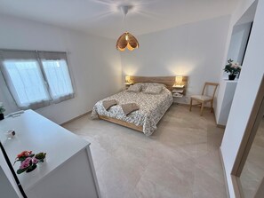 A bedroom with a bed, bedside tables, a chair, a desk, and a hanging light fixture. - Apartment with ocean view, sleeps 8 - Les Restanques (Carry-le-Rouet)