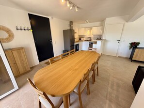 A modern kitchen with a central island, a dining area with a wooden table and chairs, and a black door. - Apartment with ocean view, sleeps 8 - Les Restanques (Carry-le-Rouet)
