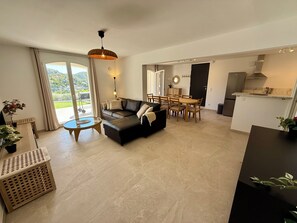 A modern living room with a sofa, dining table, and chairs, a kitchen area, and a large sliding glass door to a balcony. - Apartment with ocean view, sleeps 8 - Les Restanques (Carry-le-Rouet)