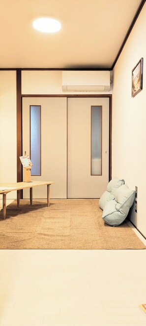 A room with a wooden table, a sofa, a wall-mounted air conditioner, and a sliding door. - なんばまで35分　門真市駅から徒歩5分　28泊以上で60%off　大型モール、コストコ、映画館が徒歩5分 (Kadomashi)
