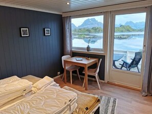Habitación de hotel con cama, escritorio, silla y vista a un cuerpo de agua y montañas.