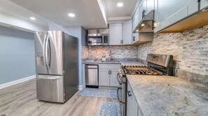 A modern kitchen with stainless steel appliances, a brick backsplash, and a wooden floor. - Spacious Newly Renovated Scenic Bay View Home Sleeps 1-8, Free Parking very safe (Ventnor City)