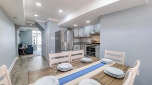 A modern kitchen with stainless steel appliances, a dining area with a wooden table and chairs, and a blue-striped runner. - Spacious Newly Renovated Scenic Bay View Home Sleeps 1-8, Free Parking very safe (Ventnor City)
