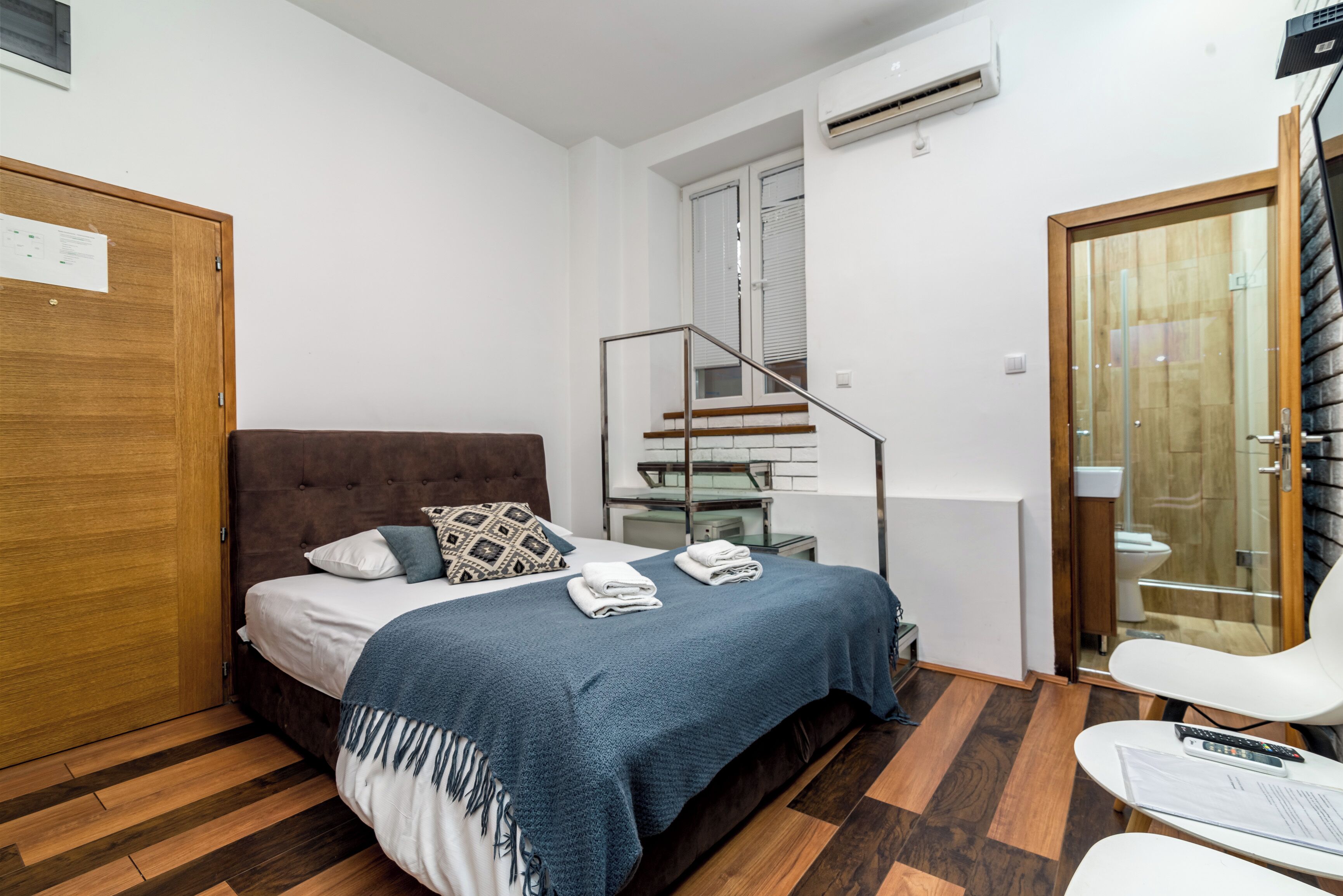 A bedroom with a bed, a wooden wardrobe, a bathroom with a toilet and shower, and a staircase.